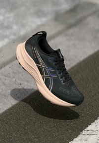 Melni skriešanas apavi ar sietu augšdaļu, rozā vidusdaļu un redzamu želejas amortizāciju. Iekļauj kontrastējošas baltas un zilas akcentus un teksturētu zoli.