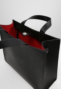 Czarna skórzana torba tote z czerwonym wnętrzem. Posiada dwa solidne uchwyty i zatrzaskowe zapięcie. Gładka tekstura, prostokątny kształt, minimalistyczny design.