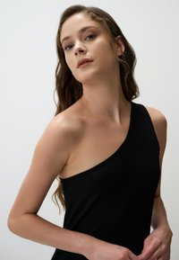 Top nero a coste con un design aderente. Tessuto liscio, forma minimalista e senza motivi visibili o dettagli in metallo.