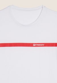 Camiseta blanca de algodón con cuello redondo, que presenta una franja horizontal roja y texto del logo en rojo en el pecho. Textura suave.