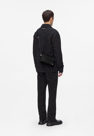 Black tweed suit set with white flecks, tailored fit. Model wears a black crossbody bag with a smooth texture, and black shoes. Simple design.