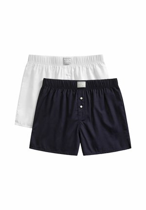 Deux paires de boxers pour hommes, un blanc et un bleu foncé, avec des ceintures élastiques et des boutons sur le devant, posés à plat sur un fond blanc.