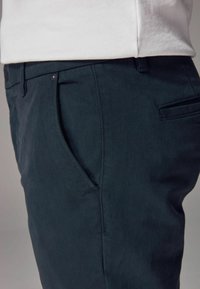 Pantalones azul marino confeccionados en tejido texturizado, con bolsillos laterales y un sutil pliegue frontal. Presenta una cinturilla estándar y detalles de costura.