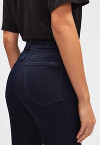 Jeans de mezclilla de color azul oscuro con cintura alta, que cuentan con bolsillos traseros y detalles de costura sutiles. Textura suave y silueta ajustada.