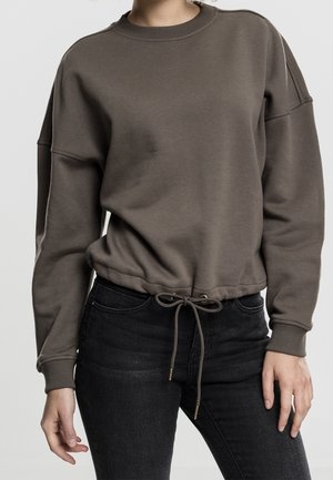 Sudadera marrón de tejido suave, con mangas largas, cuello redondo y un dobladillo con cordón. Combinada con jeans oscuros.