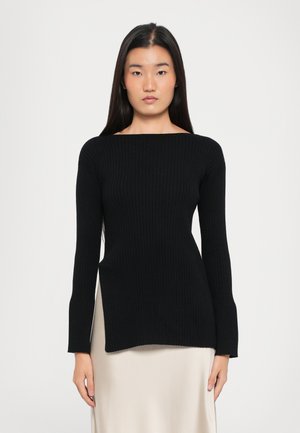 Haut à manches longues noir côtelé avec un col large et une silhouette ajustée, associé à une jupe beige lisse.
