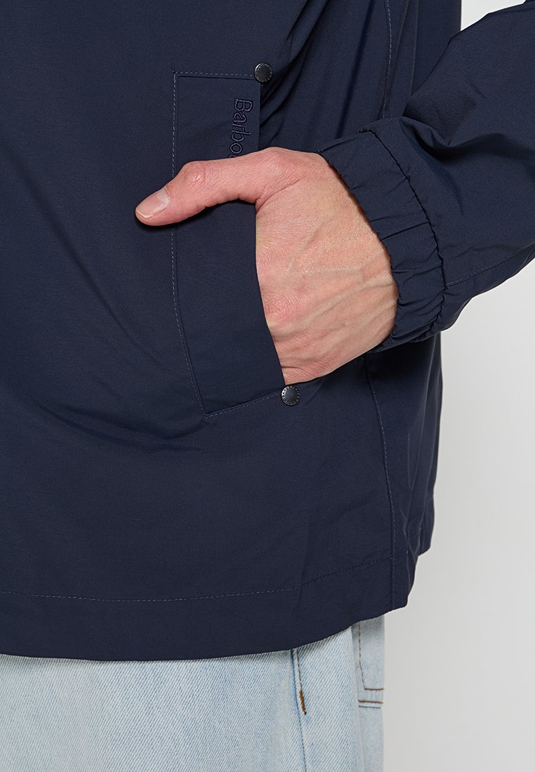 Marineblaue Jacke aus glattem Stoff, mit elastischen Bündchen, einer seitlichen Tasche mit Druckknopf und einem lockeren Schnitt.