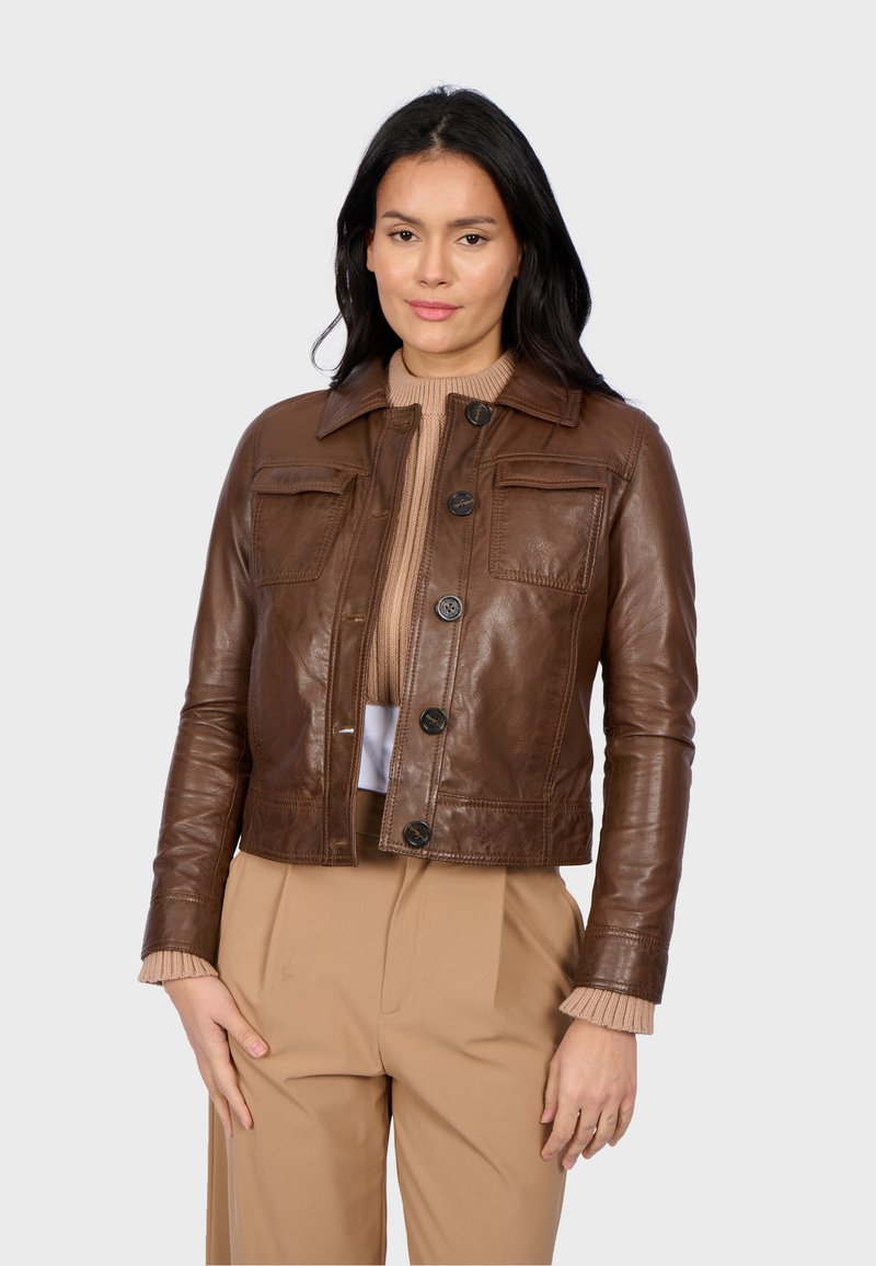 Veste cropped en cuir brun avec poches avant, col rond et boutons noirs. Portée sur un pull léger à côtes, présentée sur un fond uni.