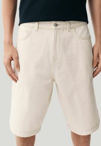 Beige Denim-Shorts mit lockerer Passform, sichtbaren Stitching-Details und einem regulären Knopfverschluss. Mit Seitentaschen und einem umgeschlagenen Saum.