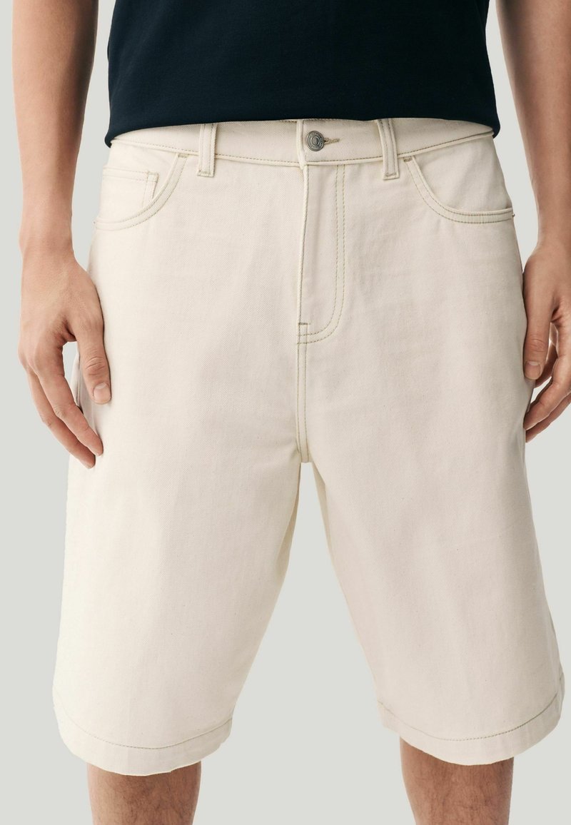 Beige Denim-Shorts mit lockerer Passform, sichtbaren Stitching-Details und einem regulären Knopfverschluss. Mit Seitentaschen und einem umgeschlagenen Saum.