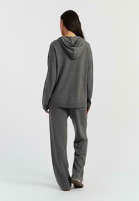 Sweatshirt à capuche gris en tissu doux, associé à un pantalon large assorti. Coupe décontractée, poignets côtelés et détails de design minimaux.