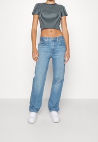 Cropad, marinblå och grönrandig t-shirt i kombination med ljusblå raka jeans. Modellen har på sig vita sneakers och står mot en neutral bakgrund.