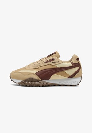Scarpa da ginnastica Puma beige e marrone con suola strutturata, chiusura con lacci e logo sul lato, mostrata su sfondo bianco.