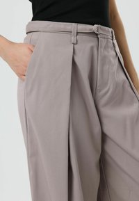 Lichtgrijze, op maat gemaakte broek met een ontspannen pasvorm, voorzien van plooien aan de voorkant, een enkele riemlus en steekzakken aan de zijkant. Soepele stoftextuur.