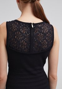 Abito nero con schiena in pizzo dal motivo floreale e paillettes. Il corpetto presenta righe testurizzate, creando un aspetto strutturato.