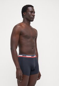 Boxers ajustados de color azul oscuro con una cinturilla a rayas en blanco y rojo que presenta el texto "Levi's". Tejido suave, diseño ajustado y longitud a mitad del muslo.