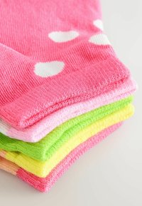 Calcetines de algodón coloridos apilados, con tonos rosa, rosa claro, verde, amarillo y melocotón. El calcetín rosa tiene lunares blancos. Textura suave.