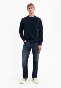 Navyblauwe gebreide sweater met geribbelde boorden en onderkant, gecombineerd met donkerblauwe jeans en witte sneakers met een blauwe accent.