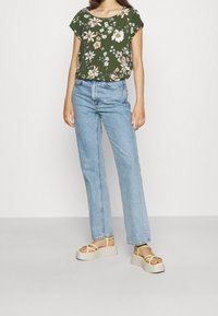 Groen topje met bloemenprint, lichtblauwe high-waisted rechte spijkerbroek en beige platformsandalen met gele bandjes. Zachte stof en losse pasvorm.