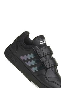 Czarne sneakersy Adidas z trzema błyszczącymi czarnymi paskami, z gładką skórzaną cholewką, wyściółką przy kołnierzu i podwójnymi rzepami. Gumowa podeszwa.
