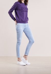 Fialová mikina s texturovaným logem "BOS" v kombinaci se světle modrými skinny džíny a bílými nazouvacími botami. Hladké materiály a přiléhavý design.