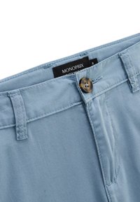 Pantalon bleu clair en tissu doux avec une fermeture à bouton et des passes de ceinture. L'étiquette affiche le nom de la marque "MONOPRIX" et la taille.