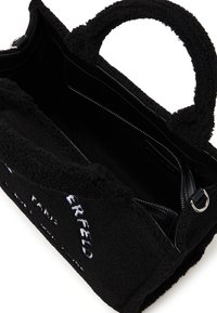 Zwarte tote bag gemaakt van textuurstof met een pluche buitenkant. Voorzien van dubbele handvatten, een rits binnencompartiment en een subtiele merkdetail.