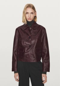 Bourgogne læderjakke med krave, knapper foran og to påsyede lommer. Har en blank overflade og et kort snit.