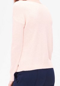 Maglione rosa chiaro lavorato a maglia con un motivo testurizzato, maniche lunghe e scollatura rotonda. L'orlo è leggermente più lungo sul retro.