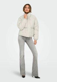 Helehall hall ploomjakk kõrge krae, tõmblukkudega taskud ja elastsete mansettidega, kantud hõlmikega hallide laiade teksade ja mustade kontsakingadega.