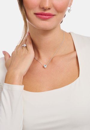 Silver necklace with a heart-shaped pendant, accompanied by matching heart-shaped earrings and a ring, all featuring clear, sparkling stones.