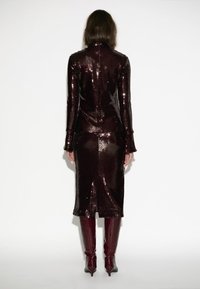 Lange bordeaux sequin jurk met lange mouwen en een zijsplit, gecombineerd met bijpassende bordeaux hoge laarzen tot de knie.