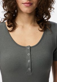 Top cinza com nervuras, de mangas curtas, decote largo e placket com cinco botões de pressão. Textura suave, design ajustado e ligeira elasticidade no tecido.