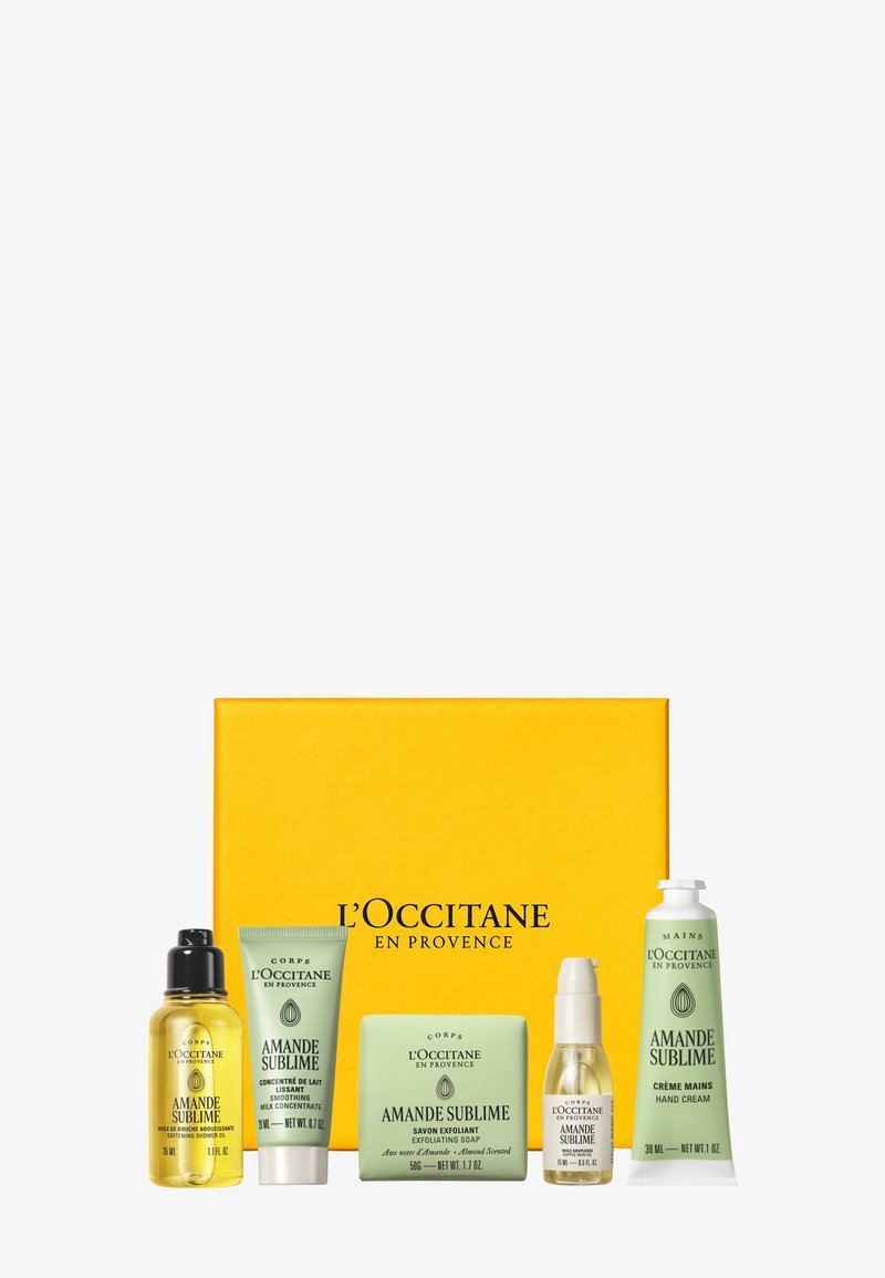 Cinque prodotti per la cura della pelle profumati alle mandorle di L'Occitane, tra cui olio doccia, latte levigante, sapone esfoliante, crema mani e olio, con una scatola gialla brandizzata.