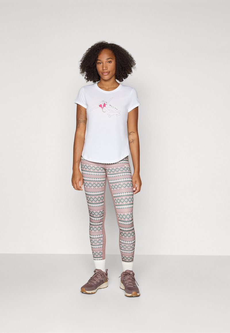 Weißes T-Shirt mit kurzen Ärmeln und einem gedruckten Design sowie rosa Akzenten, kombiniert mit gemusterten Leggings in Pastellfarben und braunen Sportschuhen.