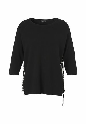 Schwarzer Pullover mit Dreiviertelärmeln, Rundhalsausschnitt und seitlichem Reißverschlussdetail, das schwarz-weiße gemusterte Stoffeinsätze zeigt.