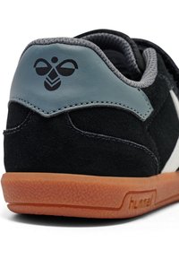 Svart mockaskor med en grå läderpanel och vita detaljer. Har en strukturerad orange gummisula och en logotyp på hälen.