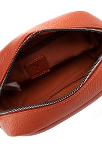 Oranje leren etui met textuur en een zwarte metalen ritssluiting, met een lege binnenkant bekleed met gladde stof en een gestikte leren label aan de binnenkant.