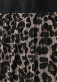 Tessuto con stampa leopardata e texture in rete nera; una cintura elastica nera con la parola "MEMORIES" in rilievo. Design plissettato con motivi a contrasto.