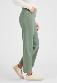 Groene high-waisted wijde broek in een katoenmix met zijzakken en gestikte accenten, gecombineerd met witte sneakers met gouden details.