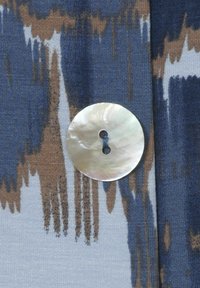 Blauwe stof met abstracte bruine en witte patronen, voorzien van een grote, ronde, iriserende schelpknop met twee knoopsgaten.
