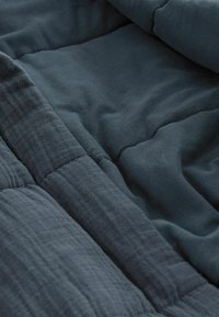 Gesteppte Decke aus dunkelblauem Stoff, mit einer weichen Textur und gestickten Mustern, die mit geschichteten Falten verschiedene Farbtöne offenbaren.