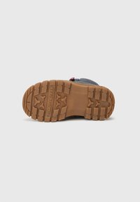 Suela de zapatilla con un material de caucho marrón texturizado y un agarre con patrón. Incluye la marca "TOMMY HILFIGER" grabada en el lado.