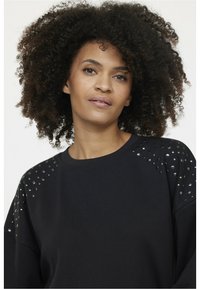 Sweatshirt noir à col rond et coupe décontractée, orné de clous métalliques aux épaules pour une touche supplémentaire. Texture lisse.