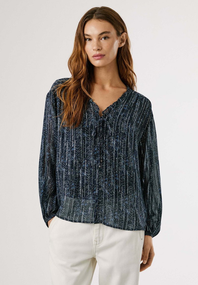 Marineblouse met verticale zilveren en blauwe strepen, voorzien van een V-hals, een strik en lange, luchtige mouwen. Gladde textuur.
