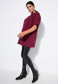 Camiseta oversize burdeos de manga corta, combinada con leggings negros brillantes y botas negras hasta la rodilla con acentos de tachuelas.