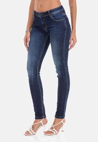 Donkerblauwe skinny jeans van denim, met een gemiddelde taille, subtiele vervaging en een klassiek vijf-pocket ontwerp, gecombineerd met witte hakken met bandjes.