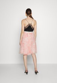 Débardeur noir à broderie en dentelle avec des bretelles fines, associé à une jupe en tulle rose, arrivant aux genoux. Comprend une taille blanche et une fermeture éclair.