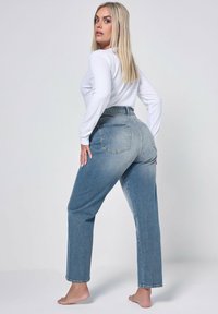 Höga ljusblå denimjeans med rak bendesign, två bakfickor och minimal blekning. Matchas med en vit långärmad topp.