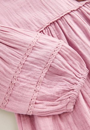 Tissu rose froncé avec une texture douce, présentant une bordure en dentelle le long des poignets de manches et du corsage, créant une apparence délicate et superposée.